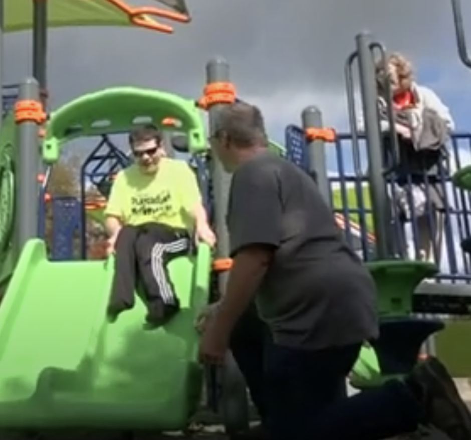 Max goes down a slide as two adults look on.
